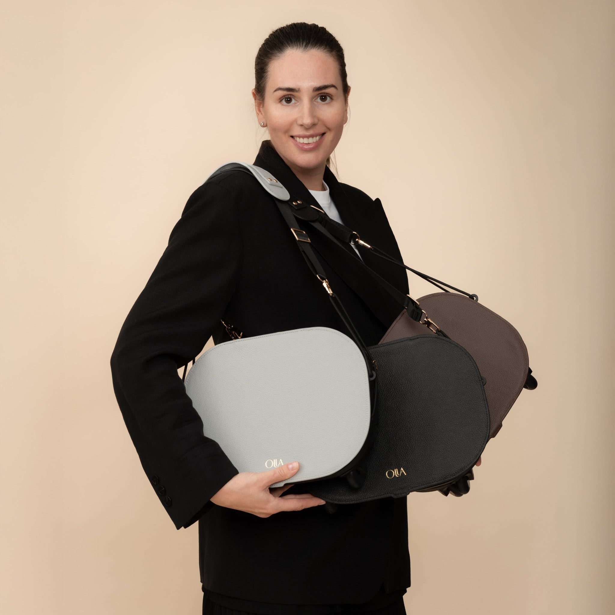 Female model holding Olla Bags in handbag configuration, displaying black, gray, and brown leather options