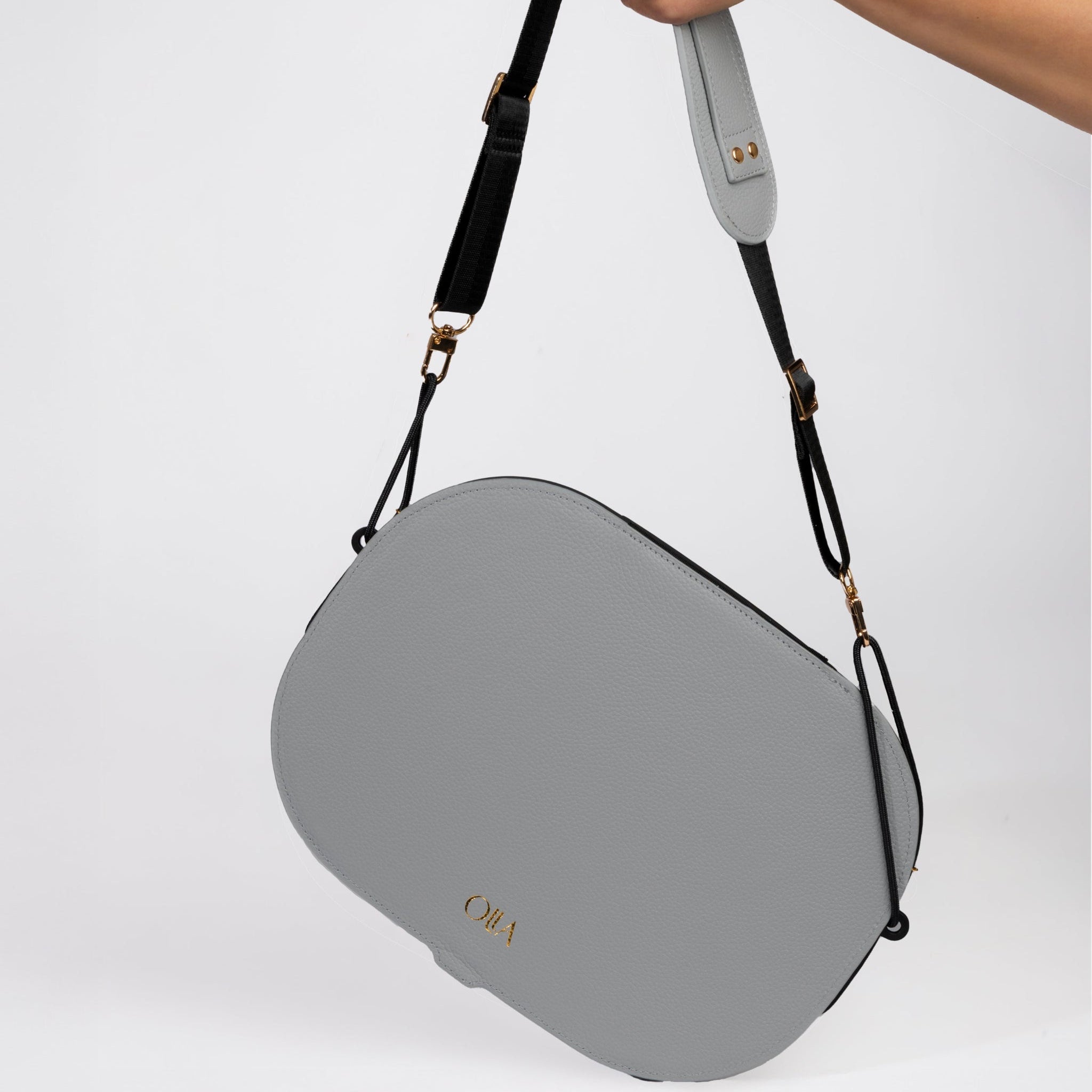 Gray handbag with a strap held by a hand on a light gray background