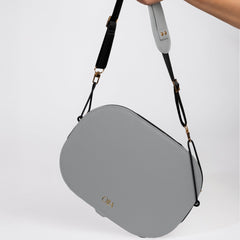 Gray handbag with a strap held by a hand on a light gray background