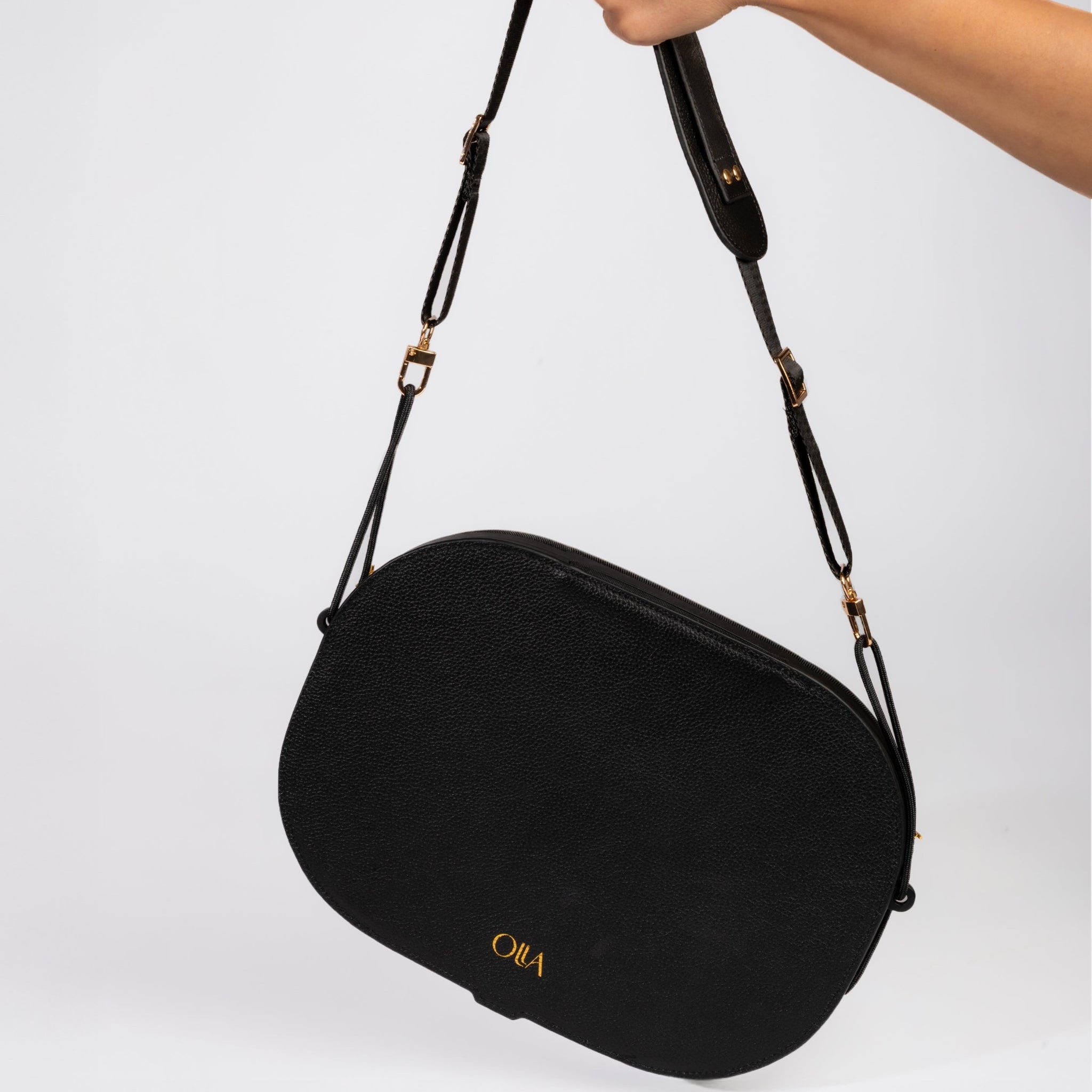 Black handbag with a strap held by a hand on a light gray background