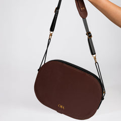 Brown handbag with a strap held by a hand on a light gray background