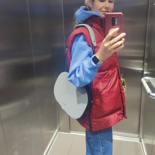 Person taking a mirror selfie in an elevator wearing a red jacket and blue shirt.