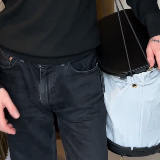 Person wearing a black sweater and blue jeans holding a black bag.