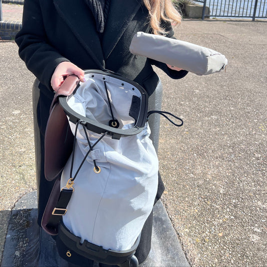 Person holding a scooter on a street with trees and buildings in the background